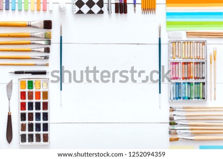 Creative art work supplies colorful accessories set on white wooden background, paintbrushes paintbox watercolors crayons pencils on artistic table, back to school. Top view, flat lay, copy space