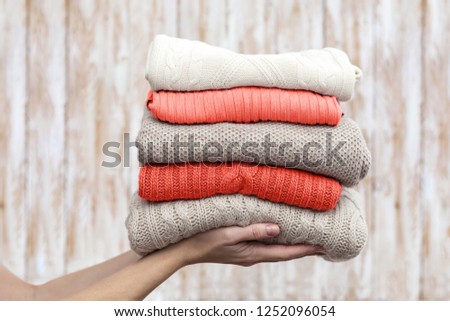 Stack of warm pastel sweaters, holding in hands. Living Coral creative and moody color of the picture.
