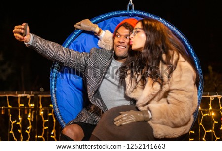 Couple sitting on swing chair and taking selfie at Christmas market, Zagreb, Croatia.