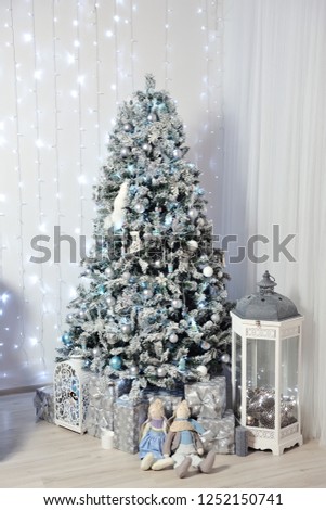 New Year's Decor in a photo studio in gray and white. A snow-white Christmas tree, gifts and lanterns, against the background of a white wall with a garland.