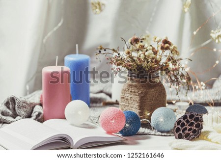 Romantic winter and New Year's style interior decoration with a candle, book, garland and dryed flowers in rustic vase
