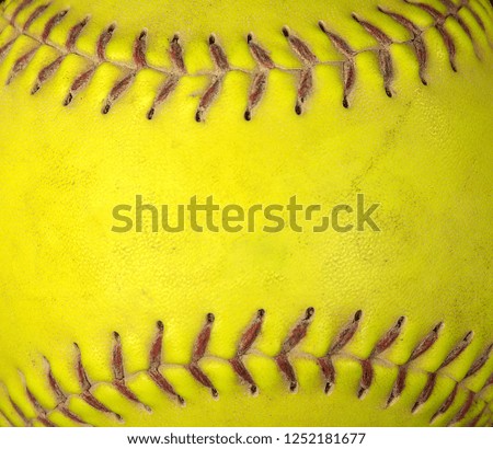 extreme close up of used neon yellow soft ball with red stitched seams