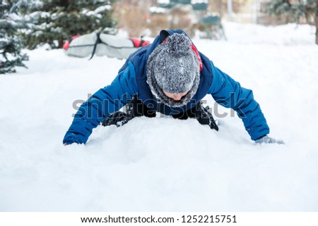 cute young boy in orange hat blue jacket plays with snow, has fun, smiles. Teenager makes snowman in winter park. Active lifestyle, winter activity, outdoor winter games, snowballs. blurred snow