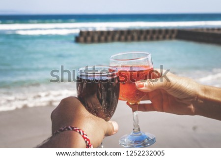 Two hands holding glasses with wine on sea background. Female and male hands with wine glasses. Bali island.
