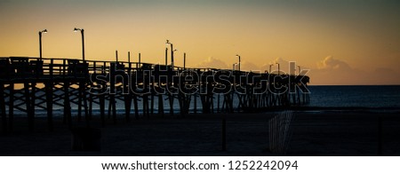 Moody picture on the beach with a long silhouette of a pier 