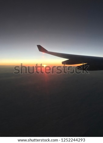 Aerial view of horizon line at sunrise seen from an aircraft, with one wing in the frame