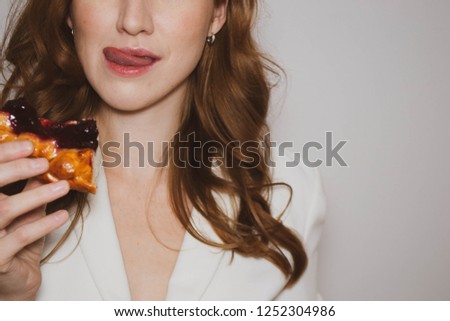 close up beautiful girl in a white jacket bites a piece of cherry pie on a white background, copy space