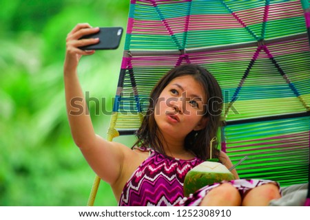 young beautiful and happy Asian Korean tourist woman drinking coconut water taking selfie picture with mobile phone at luxury tropical island resort swimming pool enjoying summer holidays 