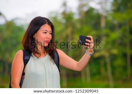 young happy and attractive Asian Chinese backpacker woman taking selfie self portrait with mobile phone at tropical island posing cheerful and relaxed exploring jungle enjoying holidays travel  