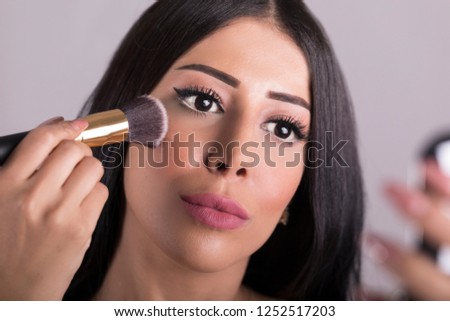 Arab Beauty woman applying makeup. Beautiful girl looking in the mirror and applying cosmetic with a big brush. Girl gets blush on the cheekbones. Powder, pink