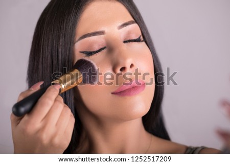 Arab Beauty woman applying makeup. Beautiful girl looking in the mirror and applying cosmetic with a big brush. Girl gets blush on the cheekbones. Powder, pink