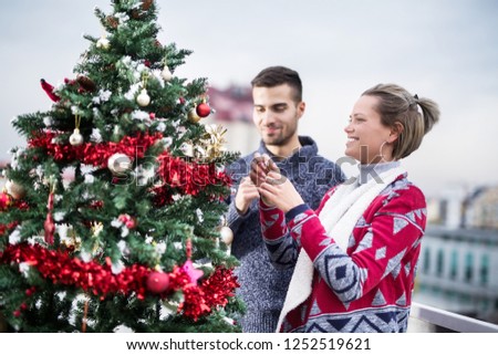Young couple decorating Christmas tree on balcony 