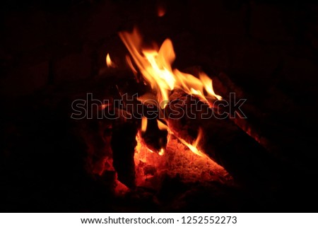 Small logs of wood burning outdoors in dark.Flames of fire against dark background creating a warm atmosphere around the campfire. photographed  at slanting angle with a fast shutter speed 