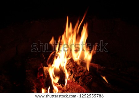Small logs of wood burning outdoors in dark.Flames of fire against dark background creating a warm atmosphere around the campfire.photographed  at slanting angle with a fast shutter speed 
