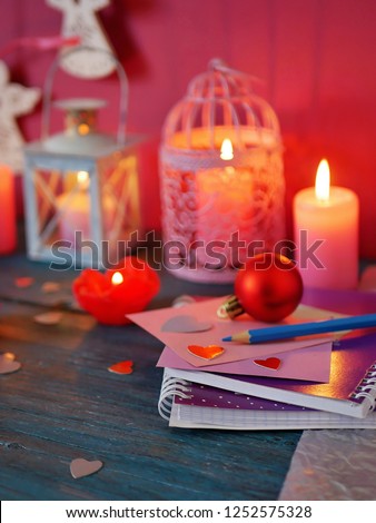 Valentine's Day decorative composition of burning candles in the form of roses, decorative lanterns with burning candles, red felt hearts, notebook and pencils, festive decor on a textural wooden tabl