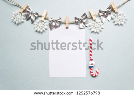 Christmas composition on a white background. Garland made of white snowflakes, silver bows and clean white paper on pastel blue background. Christmas, winter, new year concept. Flat lay