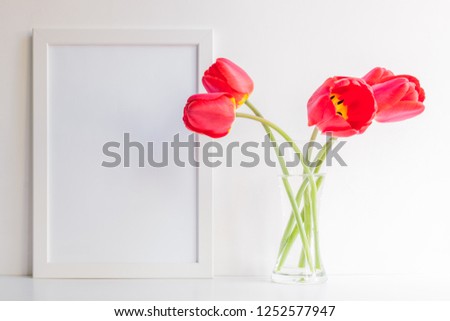 Mockup with a white frame and red tulips in a glass vase on a light background