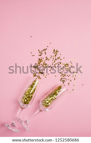 Champagne glasses with golden stars confetti on pink color paper background minimal style