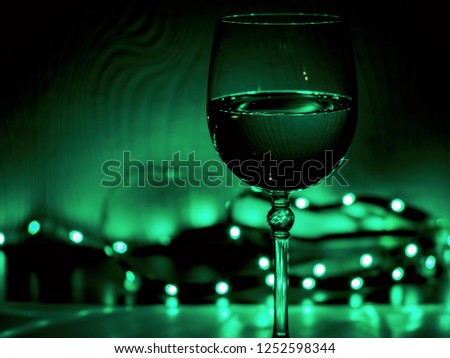 Closeup of glass of wine on the black background with Christmas decoration -bright lights. Traditional winter holiday alcohol with creative New Year artwork. Copy space. blurred or bokeh lights.