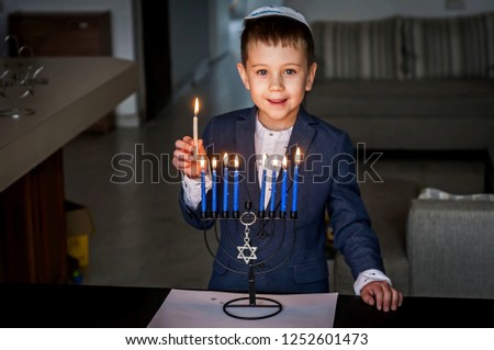 Cute Caucasian Jewish boy lighting candles on a traditional Hanukkah menorah candelabrum, Jewish holiday Chanukah concept. Royalty-Free Stock Photo #1252601473
