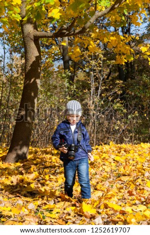 little boy in the park with a camera, enjoys photography, autumn season, Europe