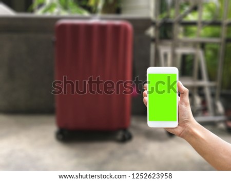 A man hand using a green screen phone to use application for travel with blurred background of luggage at hotel resort
