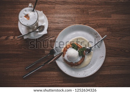 Cafe By the window daylight. Wooden table glass with white foam and cappuccino on a plate lies a round piece of cake with ice cream.
