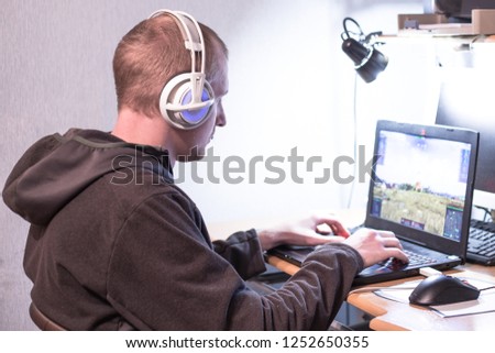 young guy in headphones sitting at the table and playing a computer game on a laptop