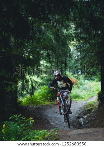 Downhill mountain bike rider jumping on mud track in green forest in the French Alps in Summer
