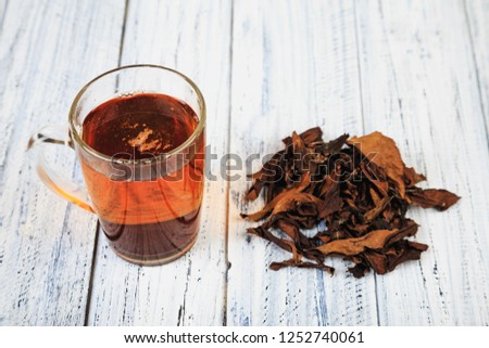 Cup of hot black tea and dried tea leaves on wooden table