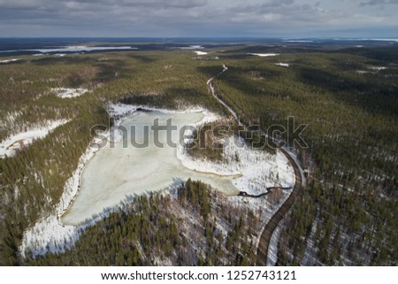 Aerial view of frozen lake and forest, road for cars winter. Photo of the northern nature of Finland with a drone. Beautiful landscape
