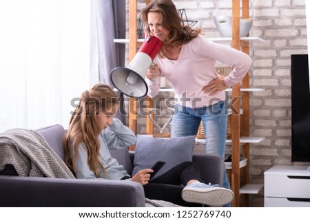 Mother Shouting Through Megaphone At Careless Girl Sitting On Sofa Using Digital Tablet