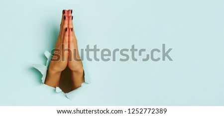 Praying hands of young woman through torn blue paper background. Christianity, church, worship concept. Banner with copy space.