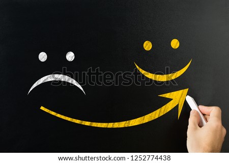 Close-up Of A Man's Hand Drawing Arrow From Sad To Happy Face On Blackboard