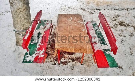 The texture and background of the old red-green arbor or benches with a table in the city in public places and courtyards against the background of fresh white snow in the daytime during the winter.