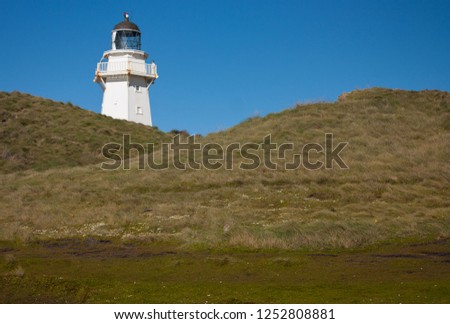 A lighthouse on a grassy hill at Waipapa Point in the South Island in New Zealand