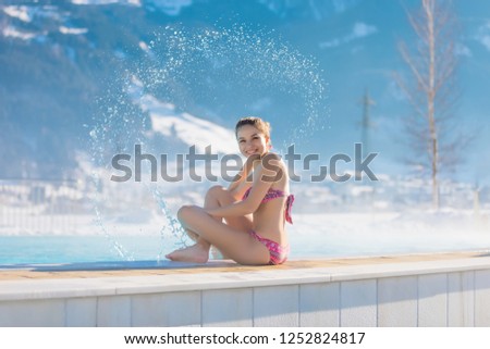 The girl sprays with water in the thermal pool. Lady sit in the open-air swimming pool with snow-covered mountains in the background. 