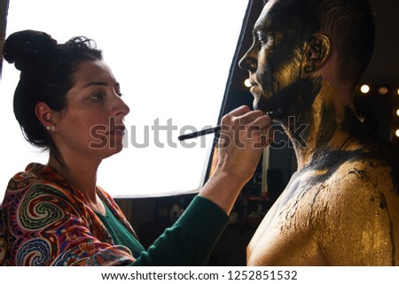 Professional makeup artist working with young man. Makeup artist working on models face in shooting break on movie set location, close-up