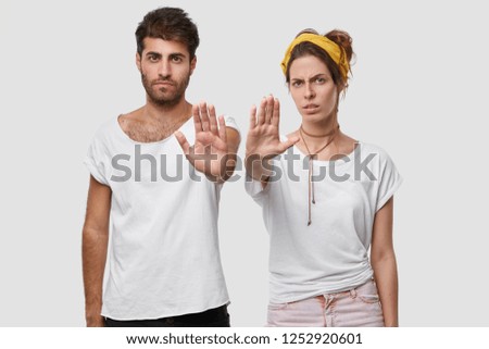 Stay away from us. Displeased young European female and male holds open palm in front of her, demand not to come close to them, make stop gesture, dressed in casual clothes. Selective focus on hands