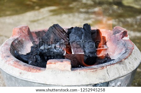 Stove, made of cement in zinc bucket, black charcoal and red fire.