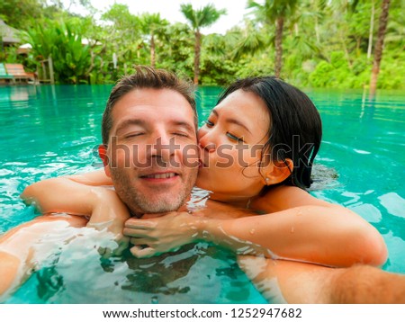 young happy and beautiful mixed ethnicity couple Asian woman and Caucasian man taking romantic selfie picture at tropical resort swimming pool enjoying honeymoon trip celebrating love