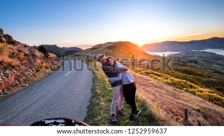 Couple enjoys beautiful Akaroa scenery near Christchurch in New Zealand. Romantic couple goes on road trip. A pair of couple goes on honeymoon in natural landscape. Happiness image of a young couple. Royalty-Free Stock Photo #1252959637