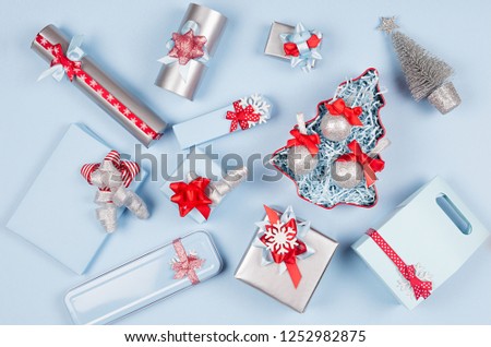 Elegance christmas silver metallic and blue paper gift boxes with red silk ribbons, decorations on pastel blue background, top view.  