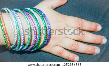 a girl child's hand wearing multi color bangles on black background 