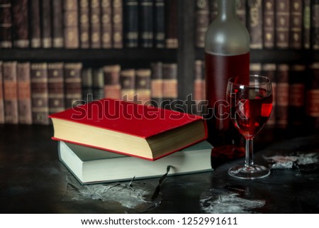in a room full of books, on the table stands a glass and a bottle of red wine, next to them lies two books