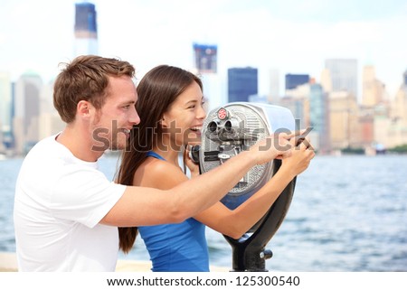 Tourists couple travel in New York. Beautiful young interracial young couple on travel looking at Manhattan and New York City skyline from Ellis Island. Asian woman, Caucasian man.
