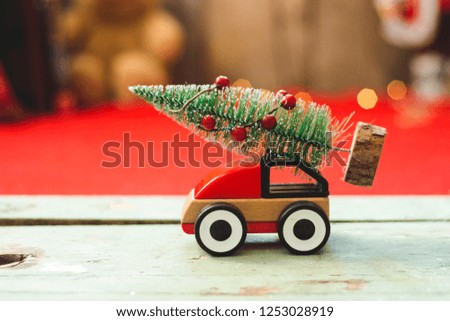 Wooden red car toy with little Christmas tree on top and Christmas decoration behind