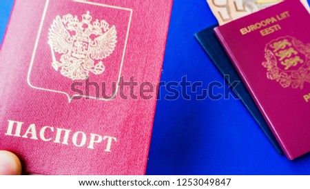 Persons hand holding passport on blue background. Citizenship of Estonia and Russia. Citizenship of European Union (EU) and Russian Federation. Top view. Copy space design. Rubles and Euro banknotes.