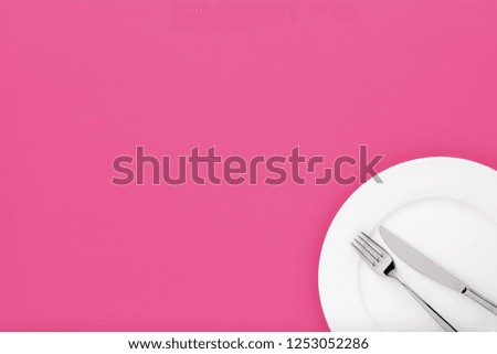 Fork and knife on white round ceramic plate on pink background with copy space. Top down view. 