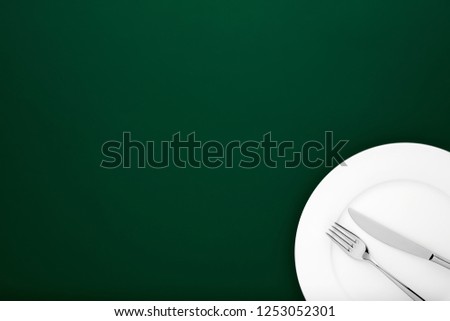 Fork and knife on white round ceramic plate on dark green background with copy space. Top down view. 